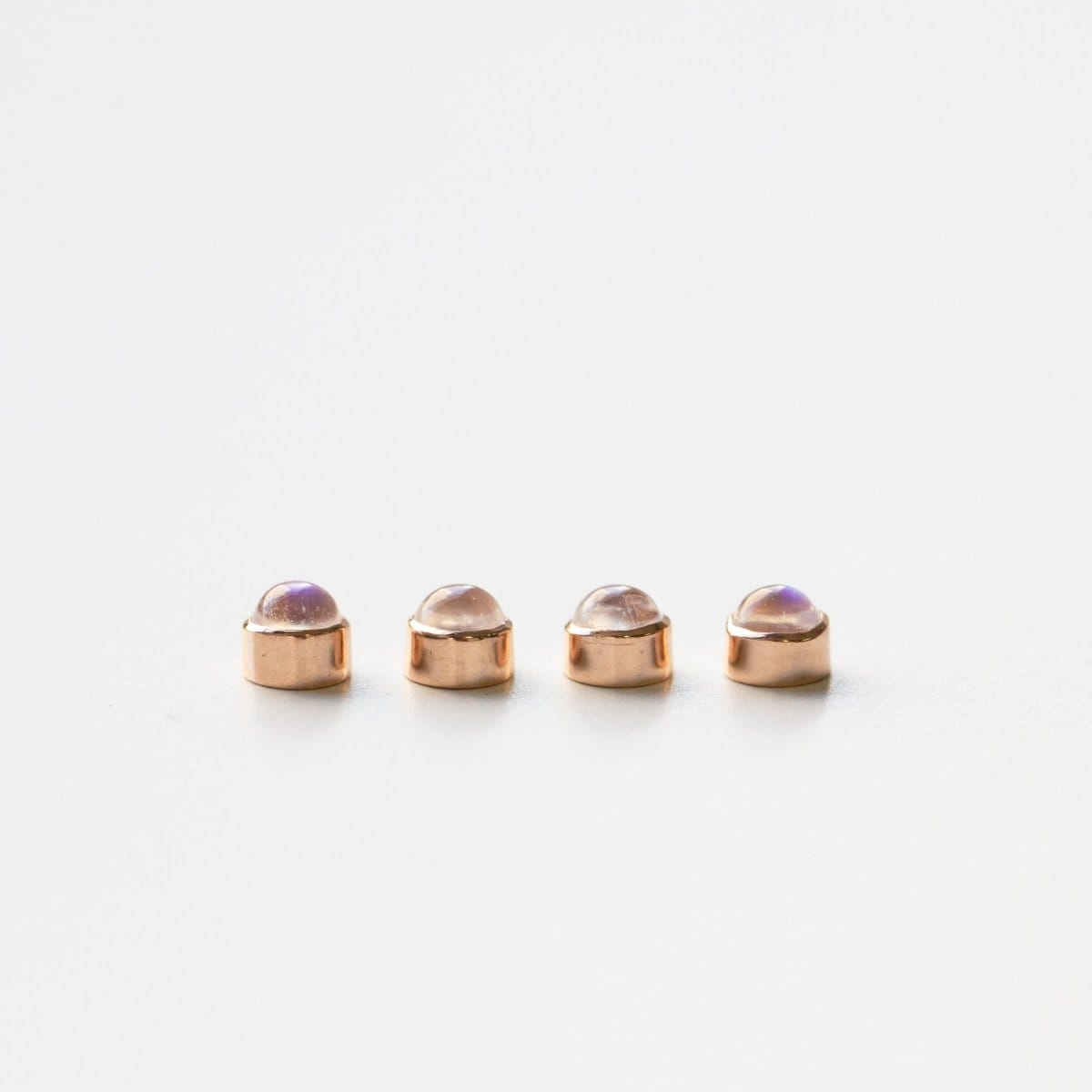 Four rose gold moonstone birthstone charms on a white background. 