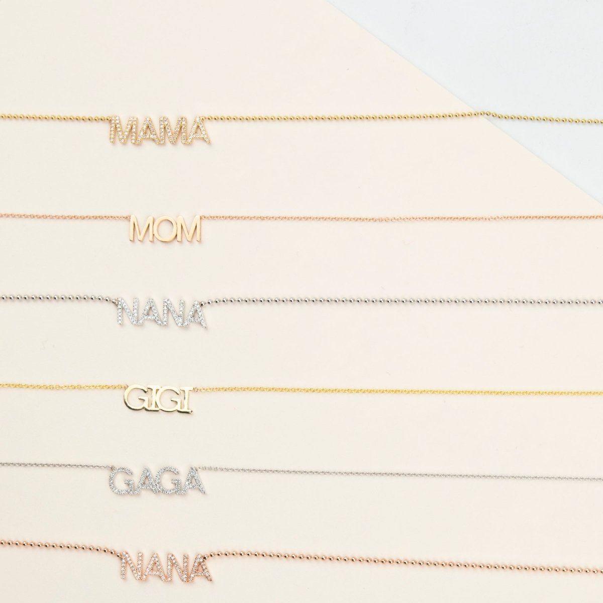 A Pavé MAMA Necklace in yellow gold, a MOM Necklace in rose gold, a Pavé NANA Necklace in white gold, a GIGI Necklace in yellow gold, a Pavé GAGA Necklace in white gold and a Pavé NANA Necklace in rose gold, against an off-white background. 