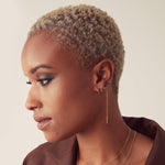 A woman wearing an Alli Webb Onyx Comfort Stud, an Onyx Threader, an Onyx Huggie and a Faceted Huggie, with short blonde hair and a brown top against a neutral background. 