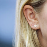 Close-up of an Open Eclipse Earring - Mini and a Solid Eclipse Earring - Mini in yellow gold in a blonde woman's ear against a blue background. 