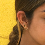 Close-up of an Open Eclipse Earring - Small and Solid Eclipse Earring - Mini in a brunette woman's ear against a yellow background. 