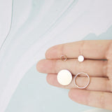 A hand holding an Open Eclipse Earring in Small and Large and a Solid Eclipse Earring in Small and Large, all in white gold, against a light background. 