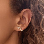 Close-up of an ear wearing a Pavé Charm Stud - Heart and a Pave Charm Stud - Moon in yellow gold. 