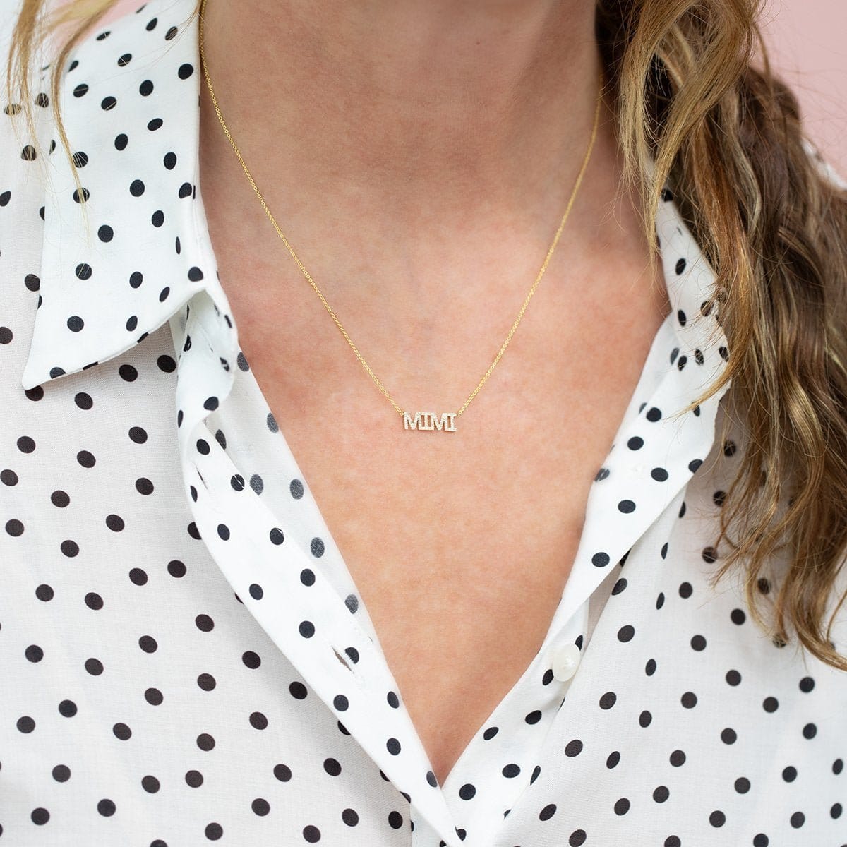 Close-up of a décolletage wearing a Pavé MIMI Necklace in yellow gold on a cable chain, with a black and white polka dot blouse and dark blonde hair visible. 