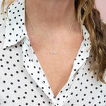 Close-up of a décolletage wearing a Pavé MIMI Necklace in yellow gold on a cable chain, with a black and white polka dot blouse and dark blonde hair visible. 