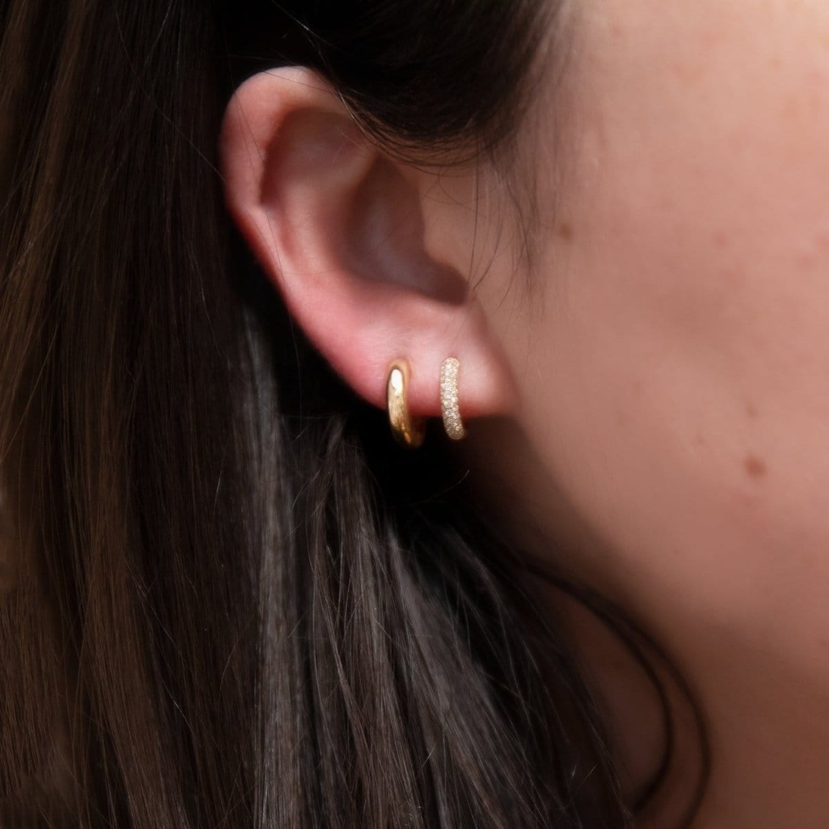 Close-up of a Gold Huggie and Pave Huggie in a brunette woman's ear. 