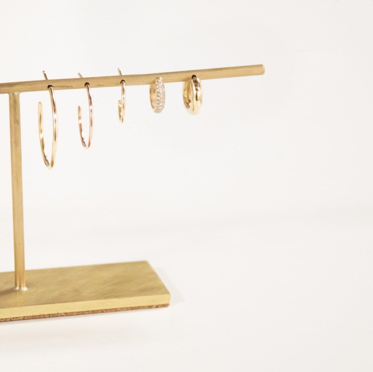 Crescent Hoops (Small, Medium, Large), a Pave Huggie and Gold Huggie on a gold earring stand against a light grey background. 