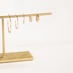 Crescent Hoops (Small, Medium, Large), a Pave Huggie and Gold Huggie on a gold earring stand against a light grey background. 