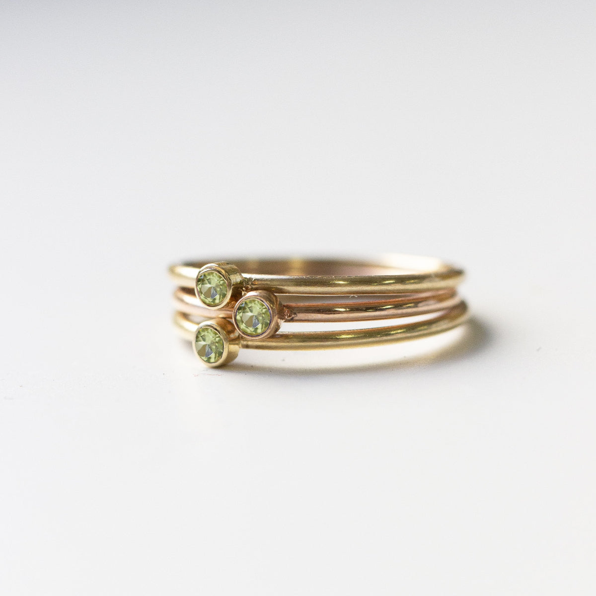 stack of 3 peridot gold rings on white background with shadow