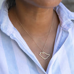 Close-up of a person's neck wearing a Saudi Arabia necklace with a blue and white striped shirt against a light grey blurred background.