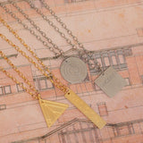 Four Virtues Pendants - Square with the word SINCERITY engraved and Circle in sterling silver, and Rectangle with the word DECISION engraved and Triangle in yellow gold vermeil on top of a page of a book with house sketches.