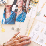 A collection of yellow gold and sterling silver jewellery from the Frank Lloyd Wright Collection x Maya, displayed with cut-out photographs and a hand wearing a Link Ring, Paris Ring, and Perla Pinky Ring.
