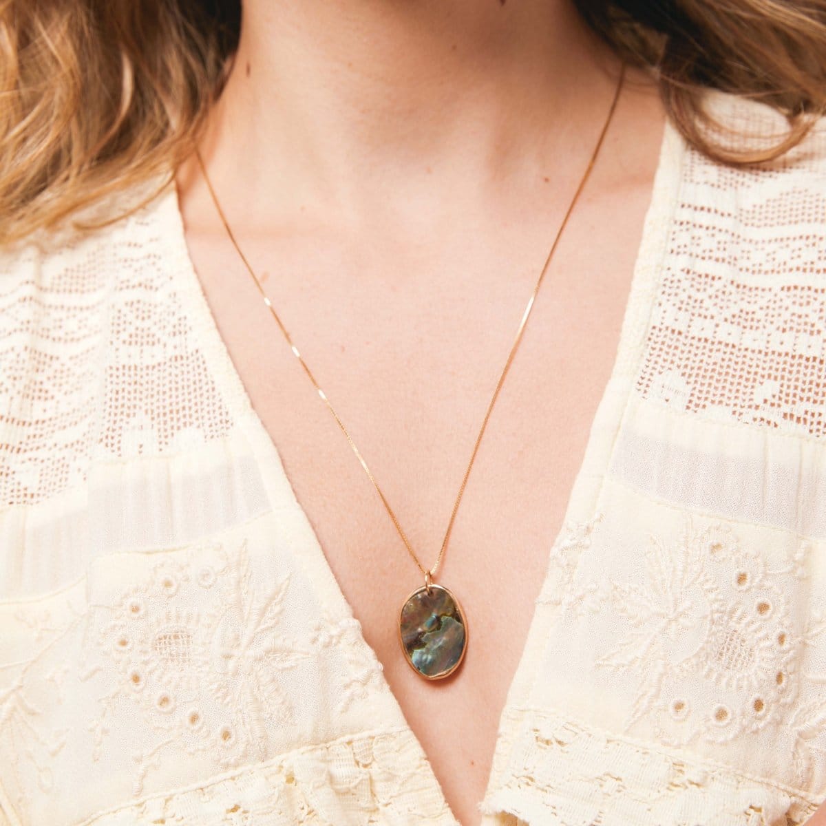 Close-up of a neck wearing The Slide Chain with a Large Abalone Cabochon Charm and a cream top. 