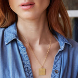 Close-up of a woman's neck wearing a Virtues Pendant - Square in yellow gold with a blue denim shirt against a blurred background. 
