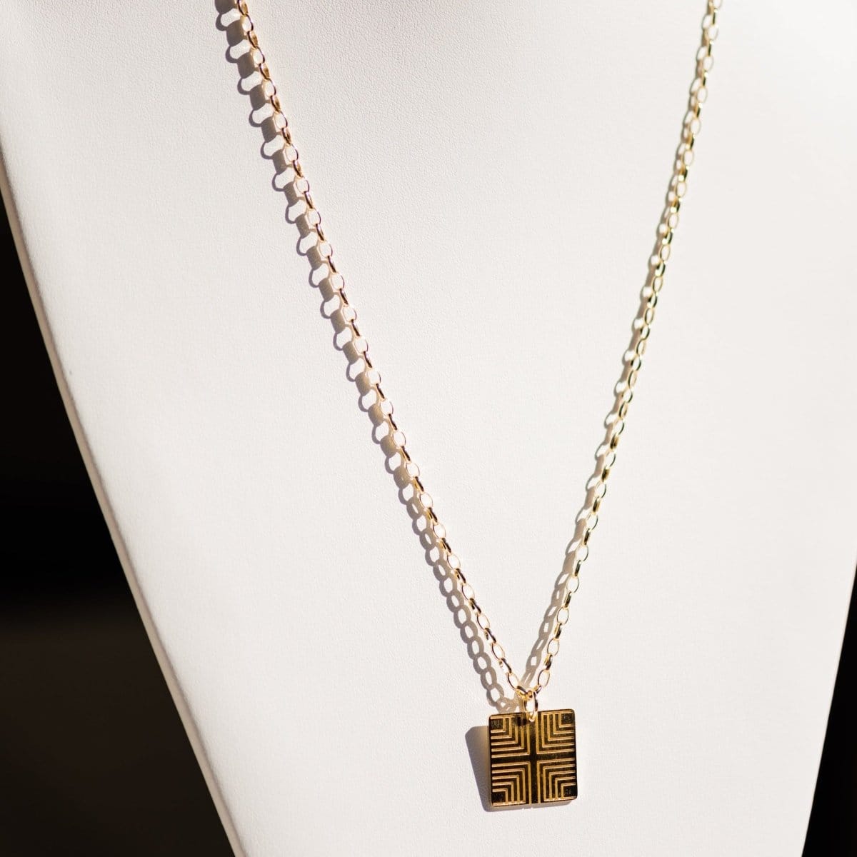 A Virtues Pendant - Square in yellow gold on a white necklace stand. 