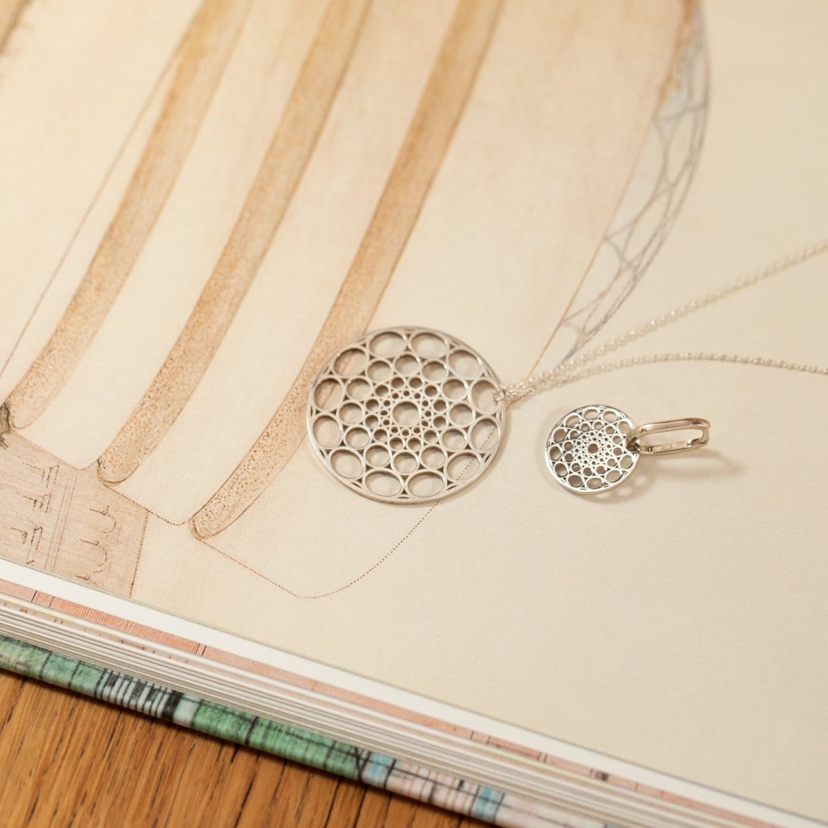 A Skylight Necklace and Skylight Hoop in sterling silver laid on top of page of a book. 