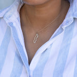 Close-up of a person's neck wearing a Sweden necklace in sterling silver with a blue and white striped shirt against a light grey background.