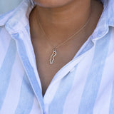 Close-up of a person's neck wearing a Sweden necklace in sterling silver with a blue and white striped shirt against a light grey background.