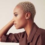 An Alli Webb Turquoise Huggie, Faceted Huggie, Opal Comfort Stud and Turquoise Threader worn by a woman with short blonde hair and a brown top against a light background. 