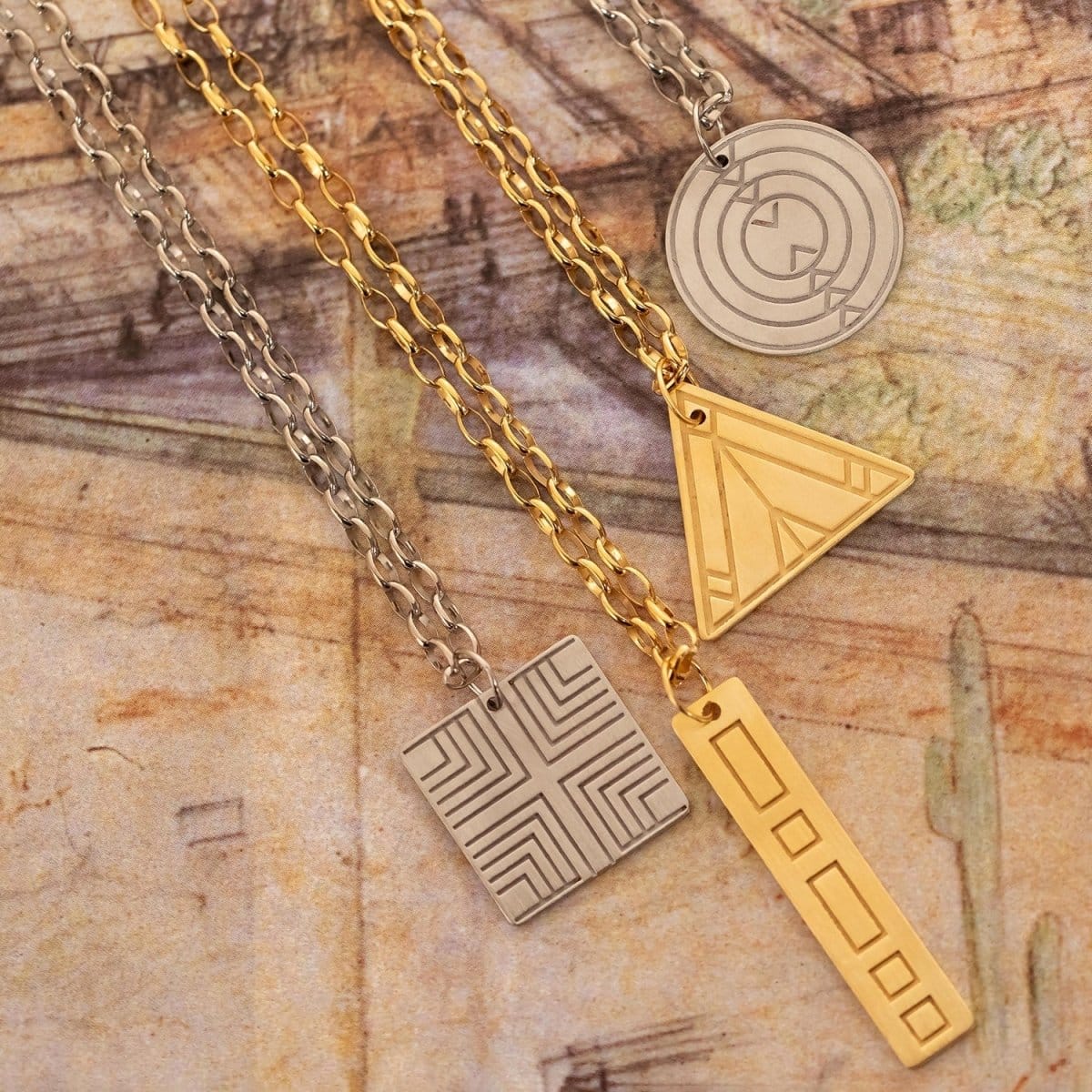 Four Virtues Pendants - Square and Circle in sterling silver, and Rectangle and Triangle in yellow gold vermeil on top of surface with different sketches. 