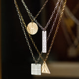Four Virtues Pendants (Circle and Triangle in yellow gold and Square and Rectangle in sterling silver) hanging against a dark blurred background. 