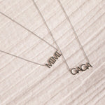 A white gold MIMI Necklace and GAGA Necklace against an off-white fabric background. 