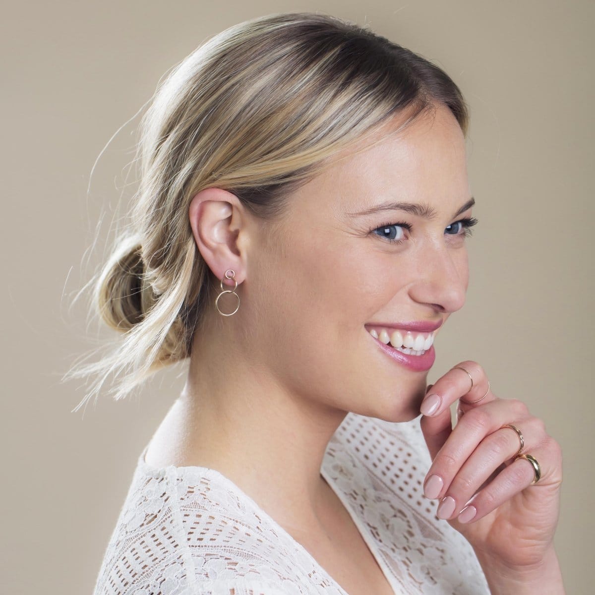 A Cascading Open Eclipse Earring, Tube Ring and Delicate Bands in yellow gold being worn by a blonde woman with a white lace top against a neutral background. 