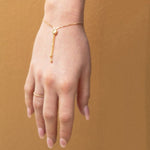 A hand facing down wearing The Slide Heart Bracelet and Delicate Beaded Band in yellow against a tan brown background. 