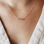 A close-up of a décolletage wearing a RESIST Necklace with a cream linen top. 