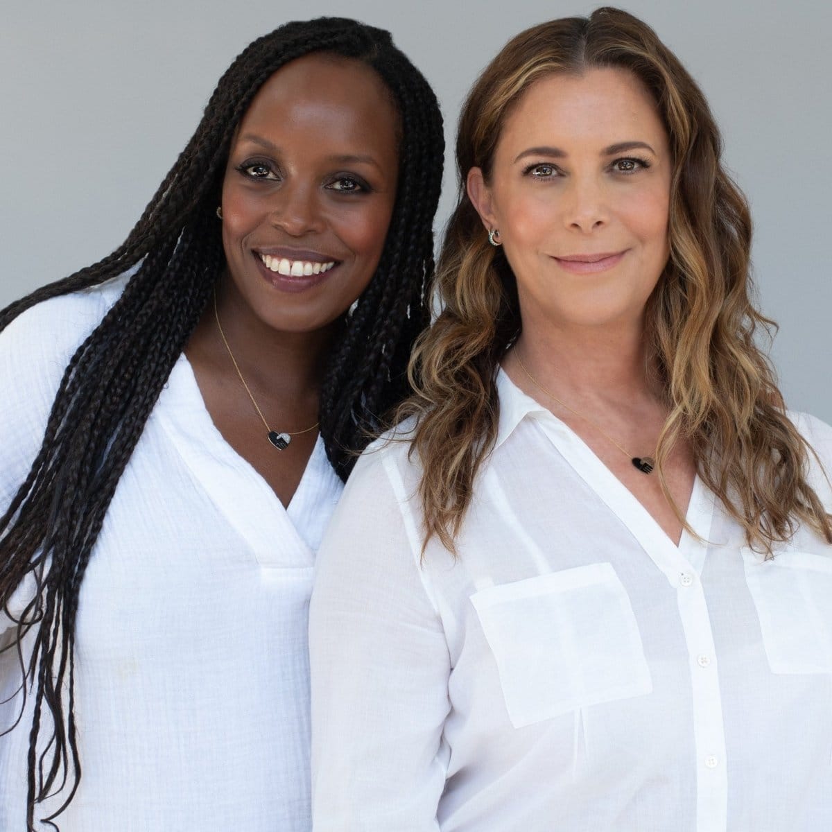 Two women each wearing Pavé Unity Pendants - Large with a white shirt against a light grey background. 