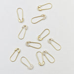 Several Gold Safety Pin Earrings and Pavé Safety Pin Earrings against a light grey background. 