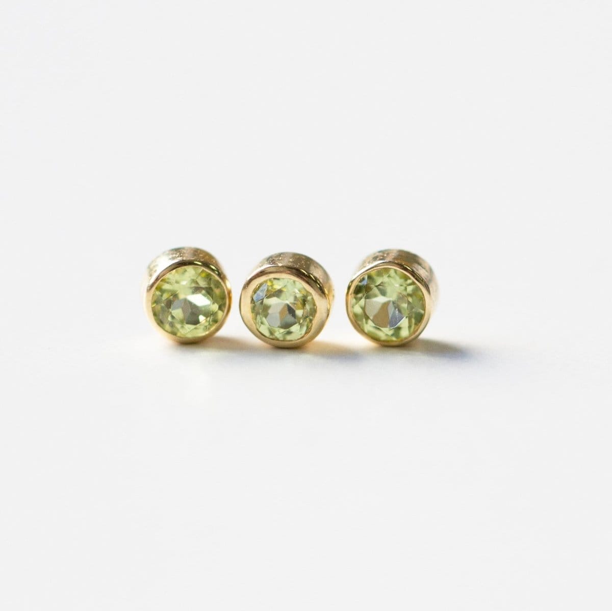 Three yellow gold peridot birthstone charms on a white background. 