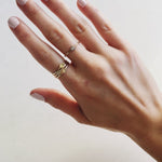 A hand wearing two Petal Rings stacked with a 14k Gold Pave Petal Ring, and a Birthstone Ring against a light grey background. 