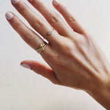 A hand wearing two Petal Rings stacked with a 14k Gold Pave Petal Ring, and a Birthstone Ring against a light grey background. 