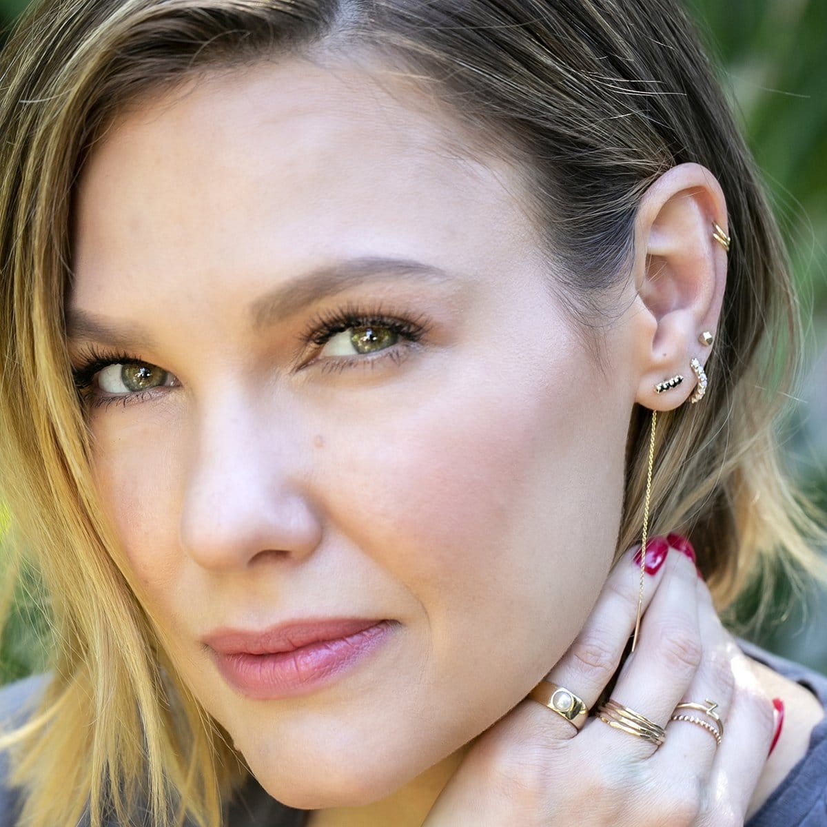 Close-up of a woman wearing an Alli Webb Faceted Comfort Stud, Onyx Threader, Opal Huggie, Rounded Ear Cuffs, Perla Pinky Ring, Flat Rings, Delicate Beaded Band, and a 14K Gold Letter Ring, with blonde hair and a blurred background.