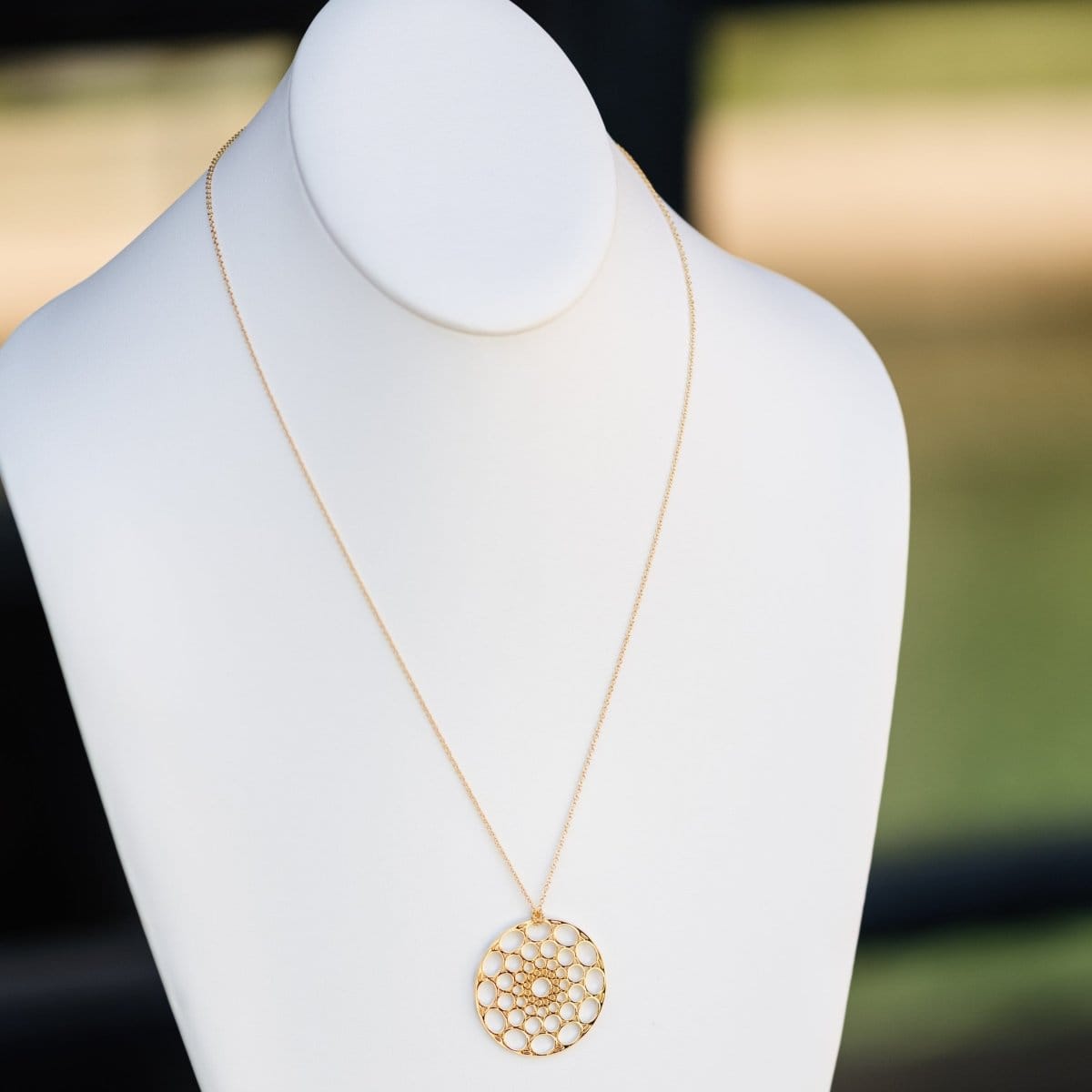 A Skylight Necklace in yellow gold on a white mannequin against a blurred background. 