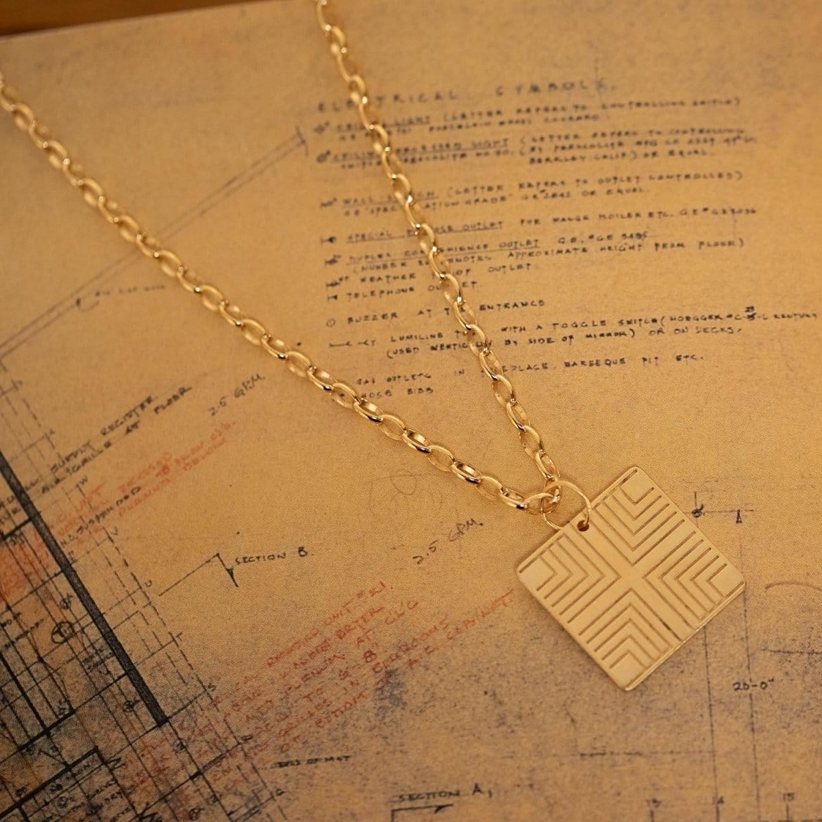 A Virtues Pendant - Square on top of a paper with sketches and writing. 