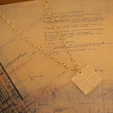 A Virtues Pendant - Square on top of a paper with sketches and writing. 