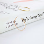 Two Crescent Hoops (one in rose gold and  one in yellow gold) on top of a white book titled Paris versus New York. 